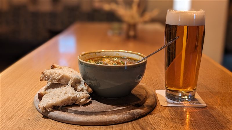 Gulaschsuppe in einer Schale mit Brot, daneben ein Glas Bier