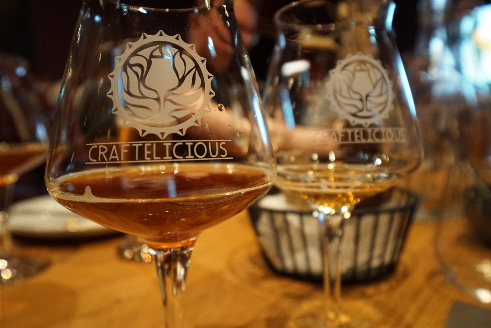 Zwei Craftelicious-Probiergläser mit unterschiedlichen Bieren auf einem Holztisch